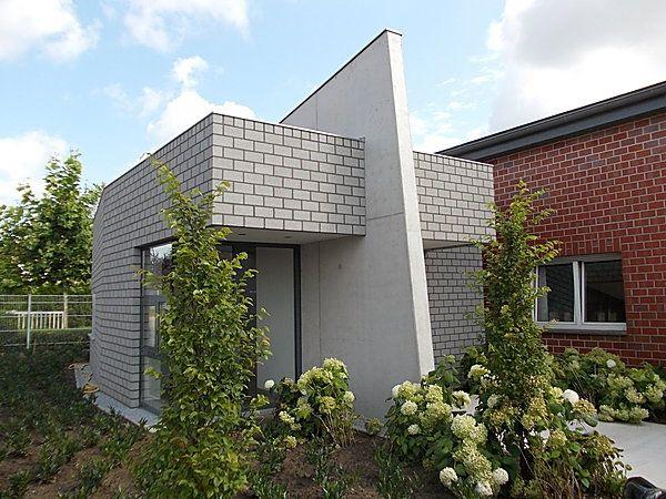 Kleines modernes Gebäude aus Betonsteinen, umgeben von Grünpflanzen und blühenden Hortensien.