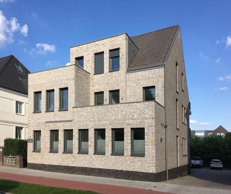 Backsteingebäude mit mehreren Fenstern und Satteldach vor blauem Himmel, moderne Architektur.