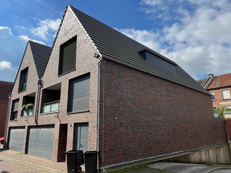 Modernes Ziegelhaus mit spitzem Dach, drei Garagentore, blaue Fensterläden unter blauem Himmel.