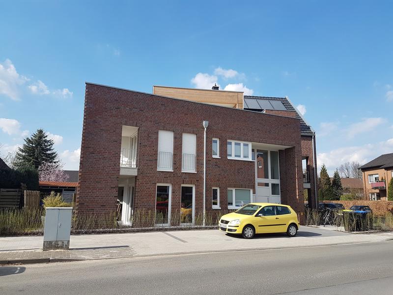 Modernes Backsteinhaus mit gelbem Auto davor, blauer Himmel, einige Sonnenkollektoren auf dem Dach.