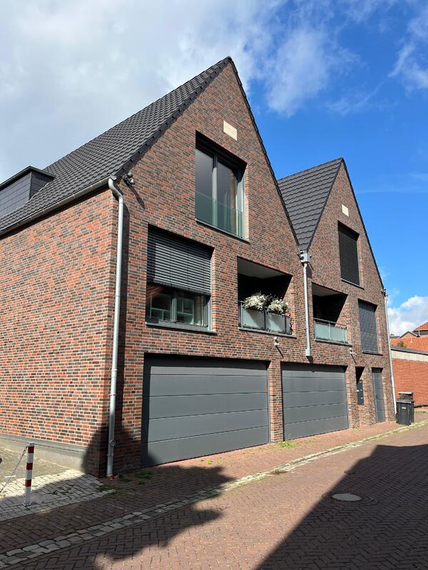 Backstein-Reihenhäuser mit dunklen Dächern, blauer Himmel, geschlossene Garagentore.