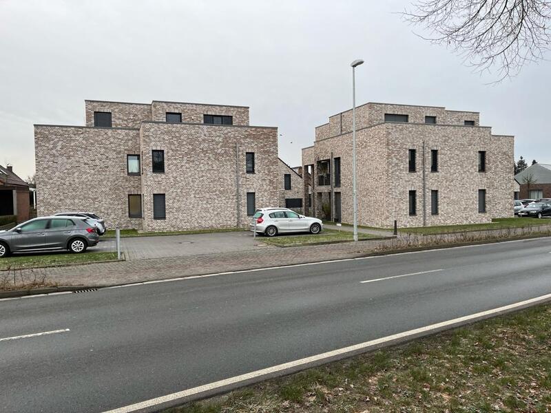 Moderne Backsteingebäude mit geparkten Autos vor grauem Himmel, Straße im Vordergrund.