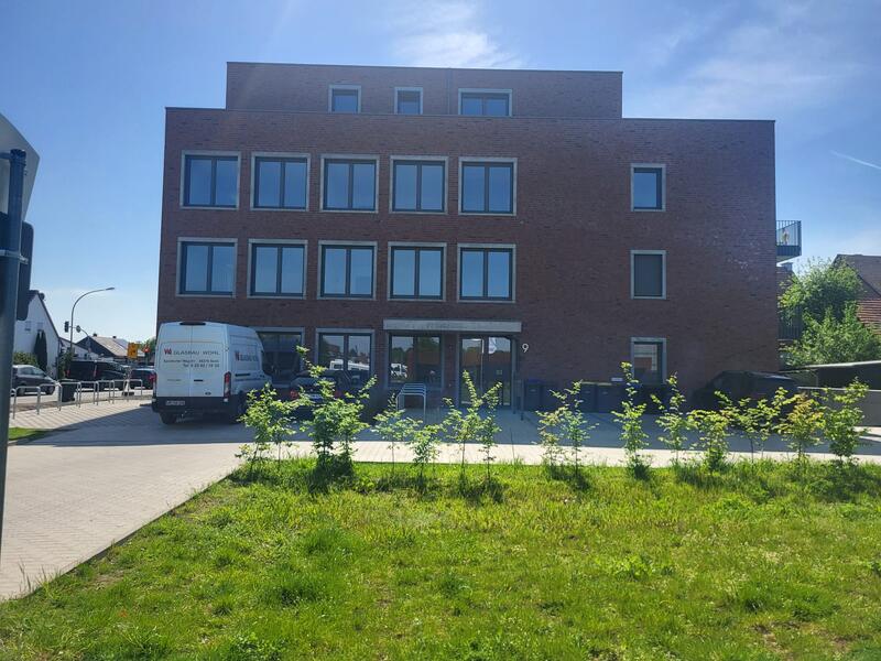 Backsteingebäude mit Fenstern, grünes Gras im Vordergrund, blauer Himmel darüber.