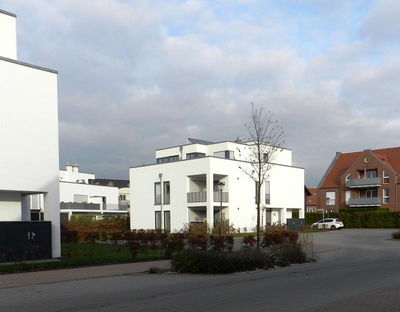 Moderne weiße Gebäude mit großen Fenstern, blauer Himmel und vereinzelter Wolken im Hintergrund.