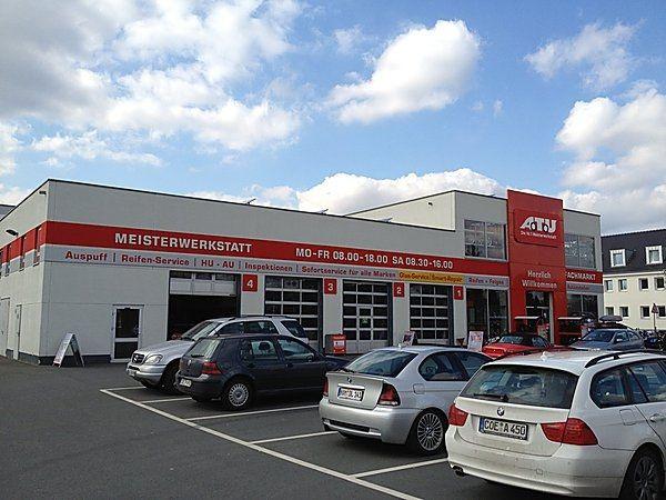 ATU-Werkstattgebäude mit roten Logos, parkende Autos, bewölkter Himmel, leuchtend rote Akzente.