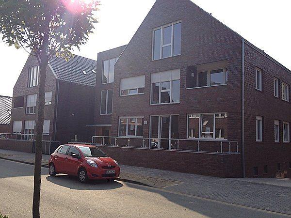 Rotes Auto vor einem modernen Backsteinhaus mit Satteldach und mehreren großen Fenstern.