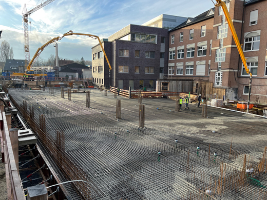 Mehrere Bauarbeiter stehen auf einer großen Baustelle vor einem Gebäude aus Backstein