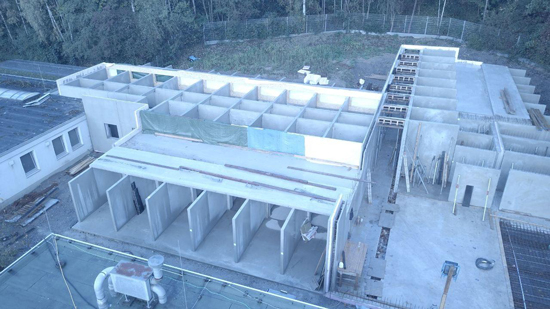 Weißes Betonbauwerk im Rohbau mit offenen Räumen und grüner Plane im oberen Bereich