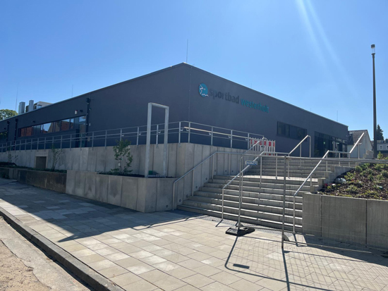 Ein modernes graues Gebäude mit großer Fensterfront und breiter Treppe im Sonnenlicht