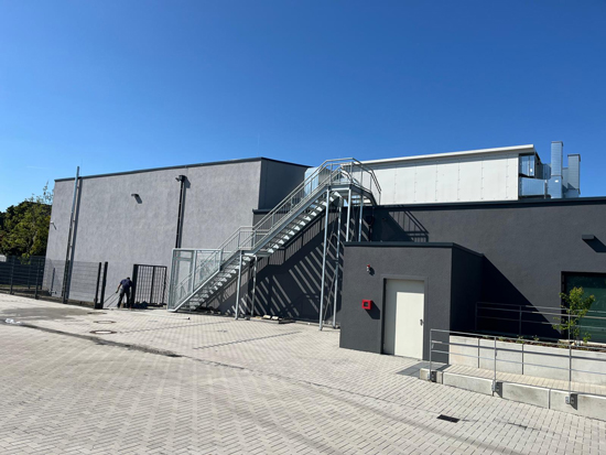 Eine Person mit dunkler Kleidung läuft an einem modernen grauen Gebäude mit Außentreppe vorbei