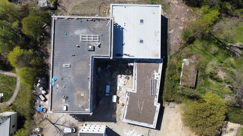 Zwei große Gebäude mit flachen Dächern umgeben von grünen Bäumen aus der Vogelperspektive