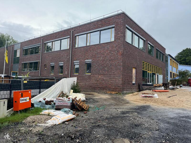 Ein modernes Backsteingebäude mit vielen Fenstern steht auf einer Baustelle mit Baumaterialien