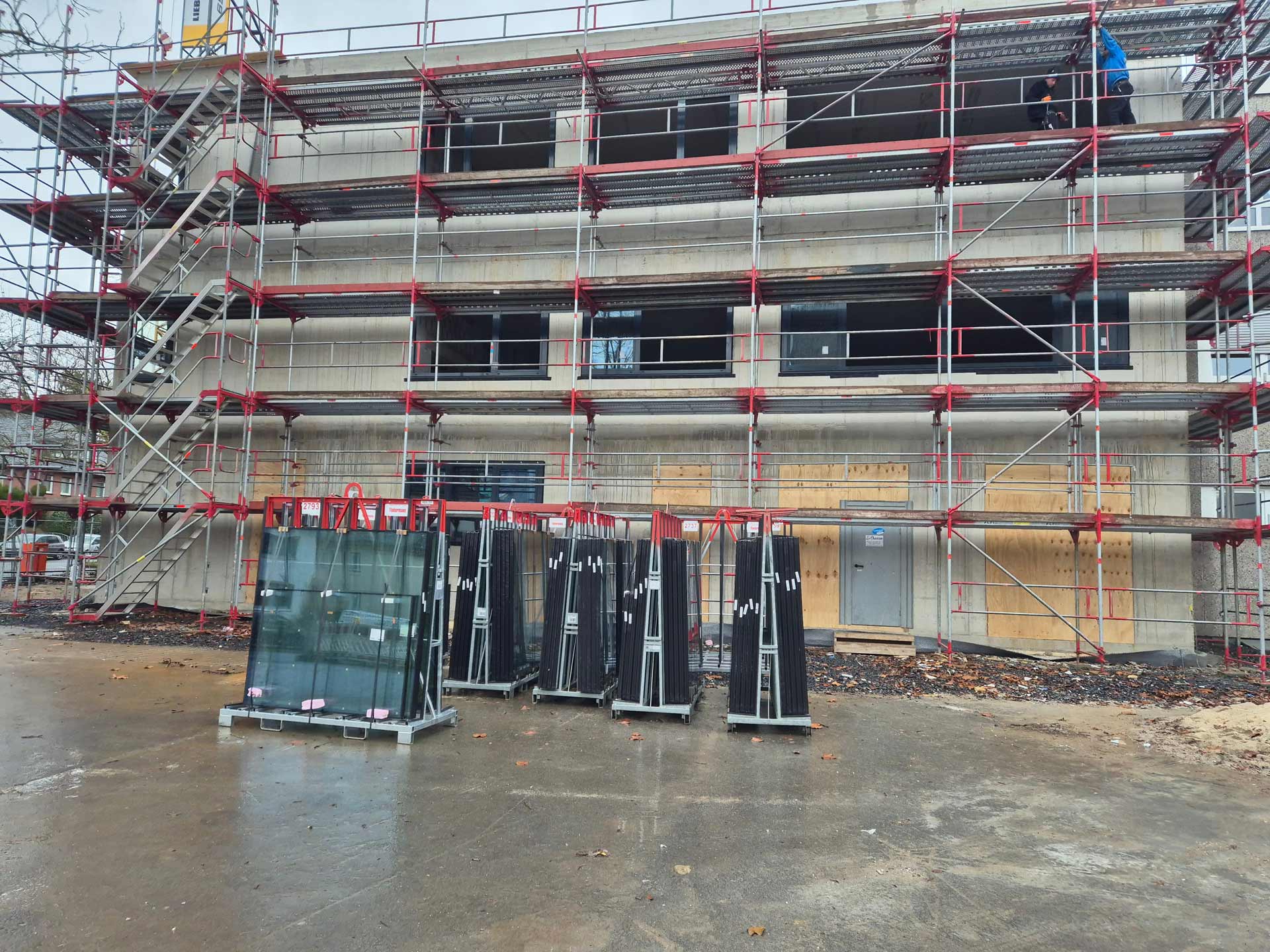 Ein Rohbau mit drei Stockwerken und rot-silbernem Baugerüst an einem grauen Tag