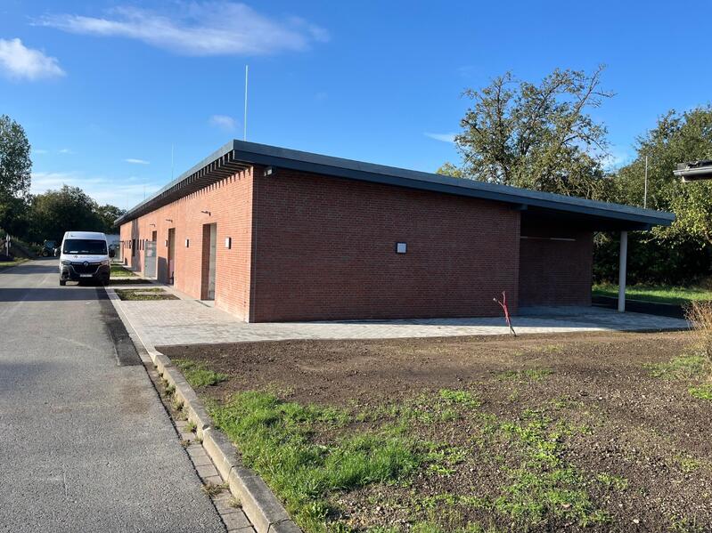 Ein langes rotes Backsteingebäude mit schrägem Dach und weißem Transporter davor