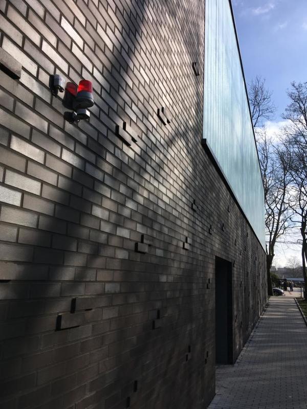 Die Backsteinwand eines modernen Gebäudes mit Überwachungskamera und Schatten von Bäumen