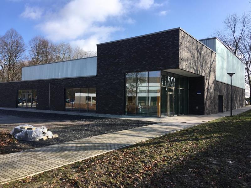 Modernes zweistöckiges Gebäude mit dunkler Klinkerfassade und Glasfront unter blauem Himmel