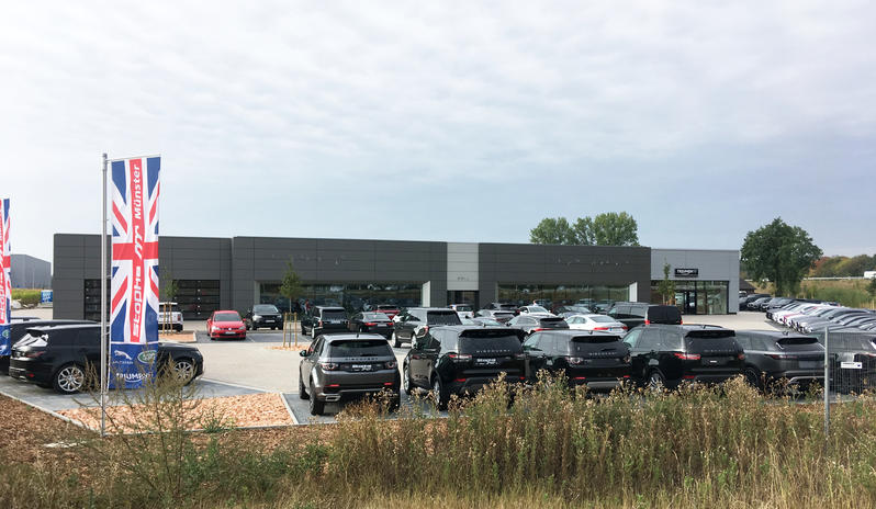 Mehrere schwarze Autos parken vor einem modernen grauen Autohaus mit großen Fenstern