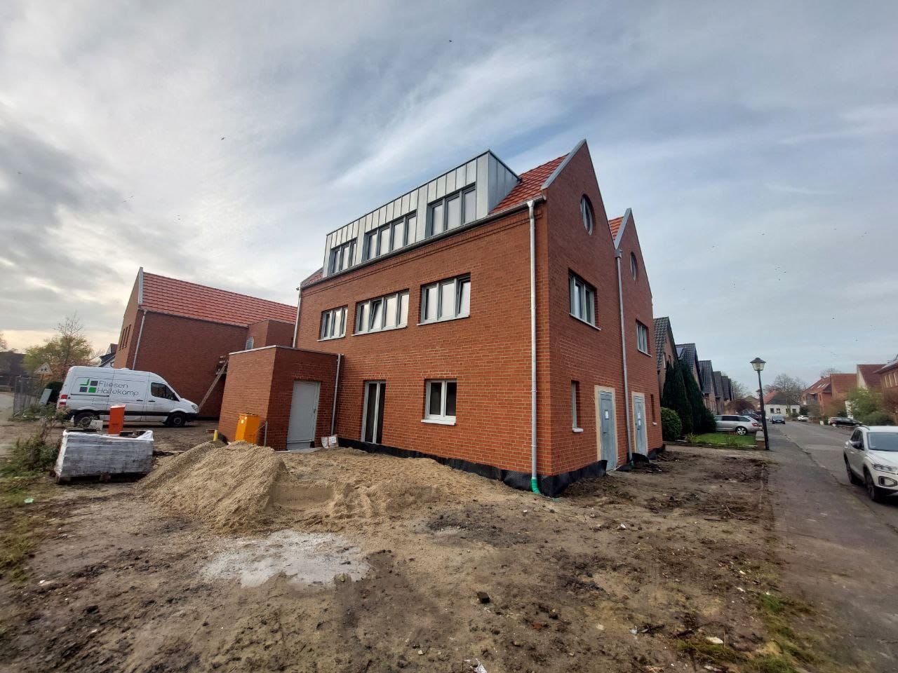 Ein rotes Backsteingebäude mit grossen Fenstern steht auf einer Baustelle im Wohngebiet