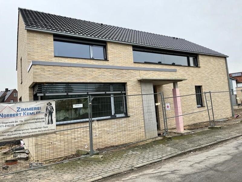 Modern zweistöckiges Haus mit beigem Klinker, großen Fenstern und Bauzaun vorne