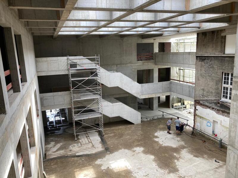 Zwei Personen stehen nachdenklich in einer großen Baustelle mit Betonwänden und Gerüst