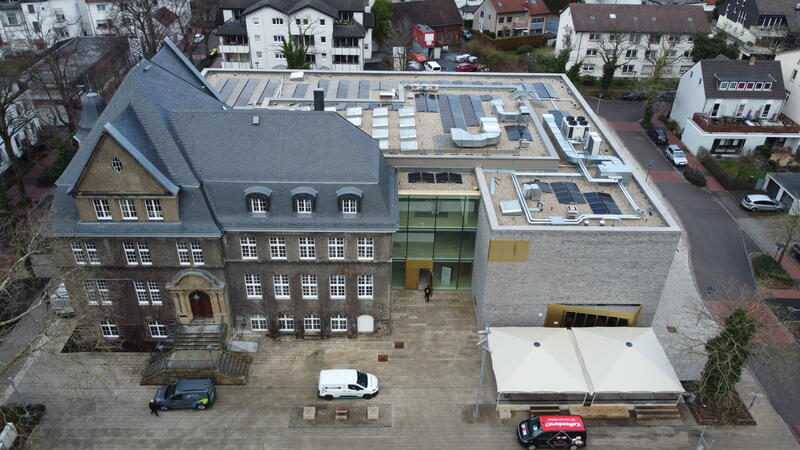 Großes altes Gebäude mit modernem Anbau und Solarpaneelen auf dem Dach in Wohngegend