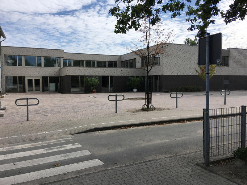 Ein modernes, hellgraues Schulgebäude mit großen Fenstern und leerem Vorplatz