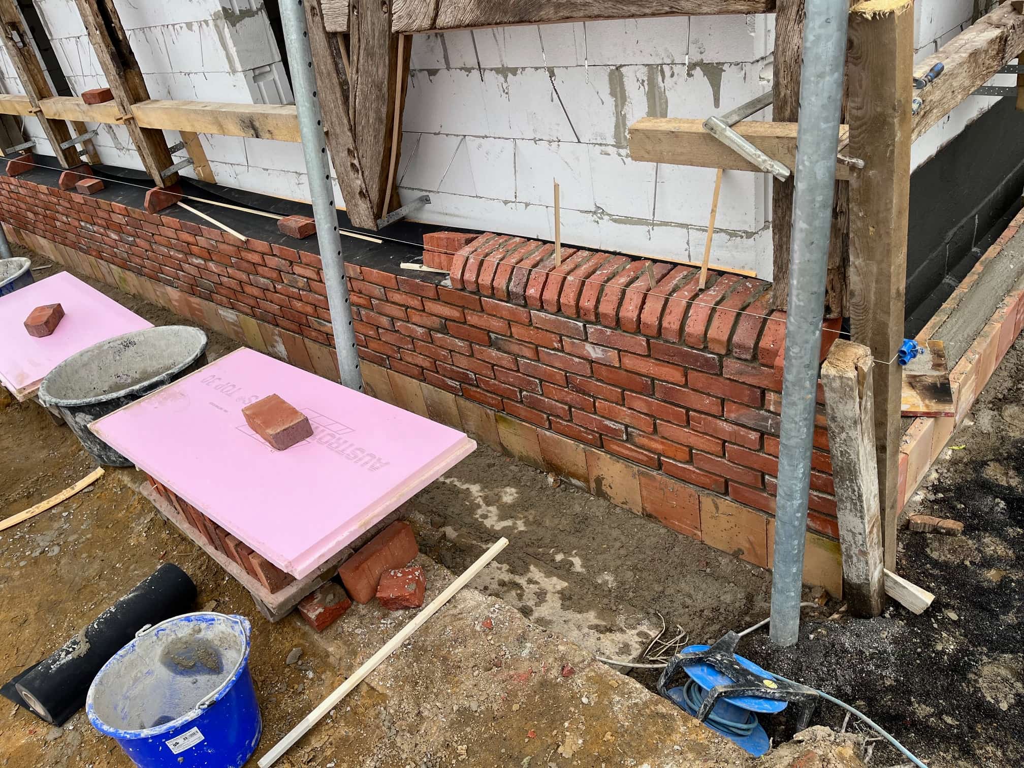 Frisch gemauerte Backsteinwand mit rosa Dämmplatten und Baumaterialien auf Baustelle