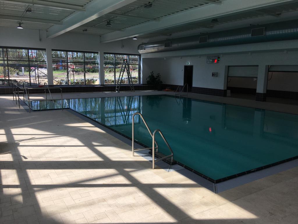 Ein leeres Hallenbad mit klarem Wasser und großen Fenstern, Sonnenlicht fällt herein