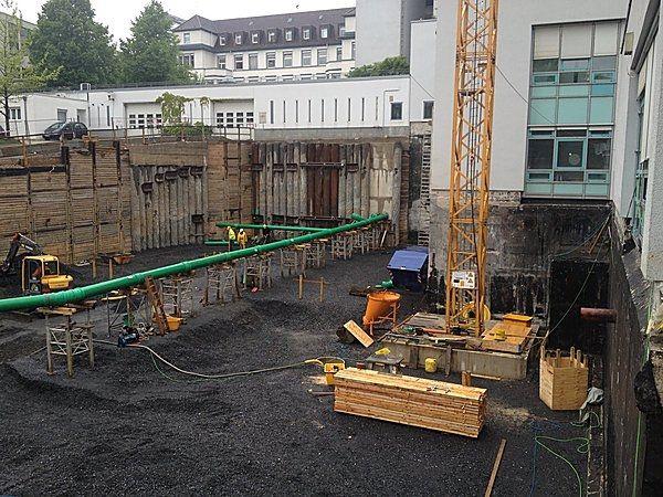 Eine Baustelle mit gelbem Kran, grünen Rohren und Holzplatten im Erdgeschossbereich