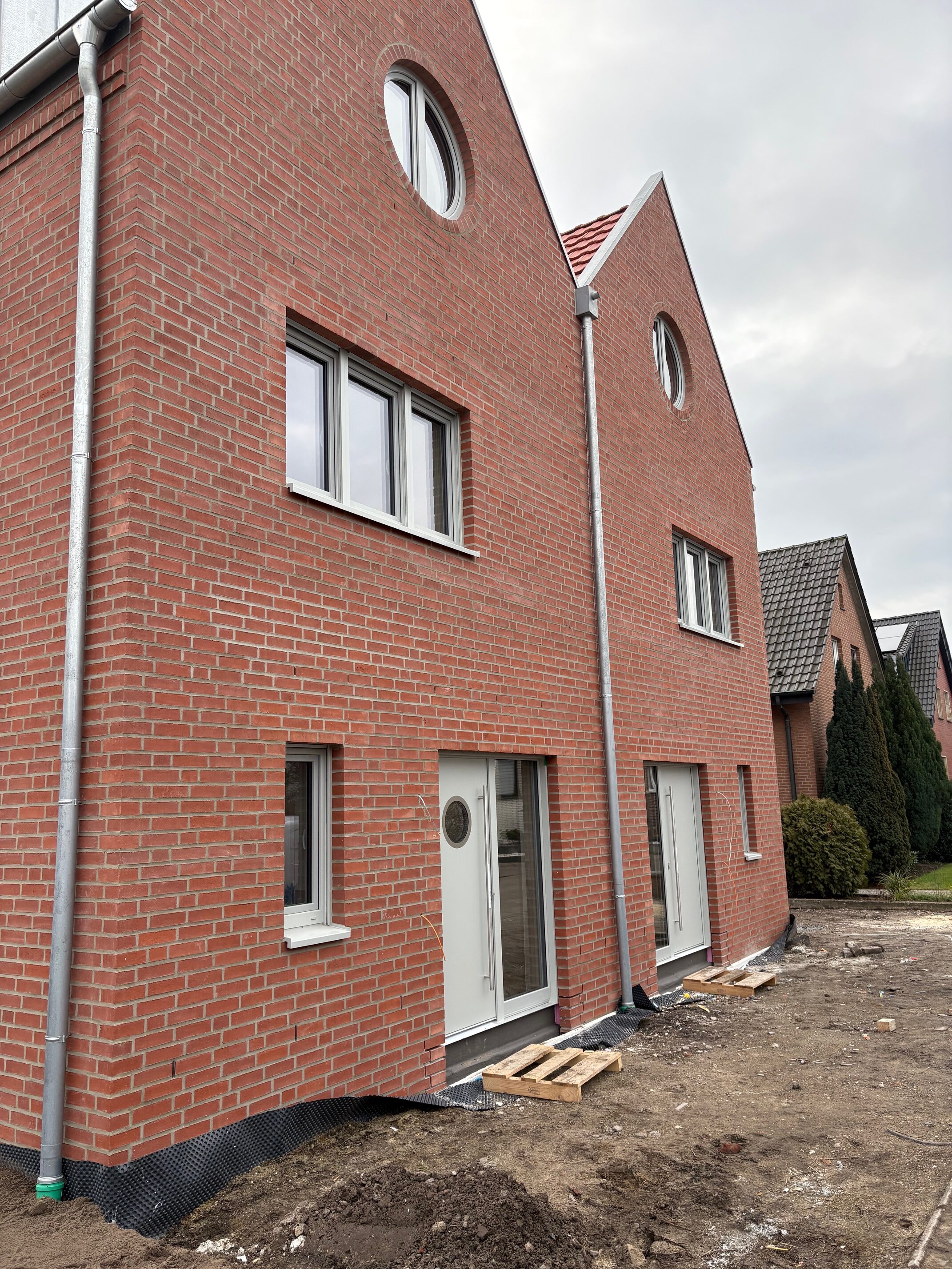 Rotes Backsteinhaus mit runden Fenstern und frischem Gartenbau vor dem Eingang