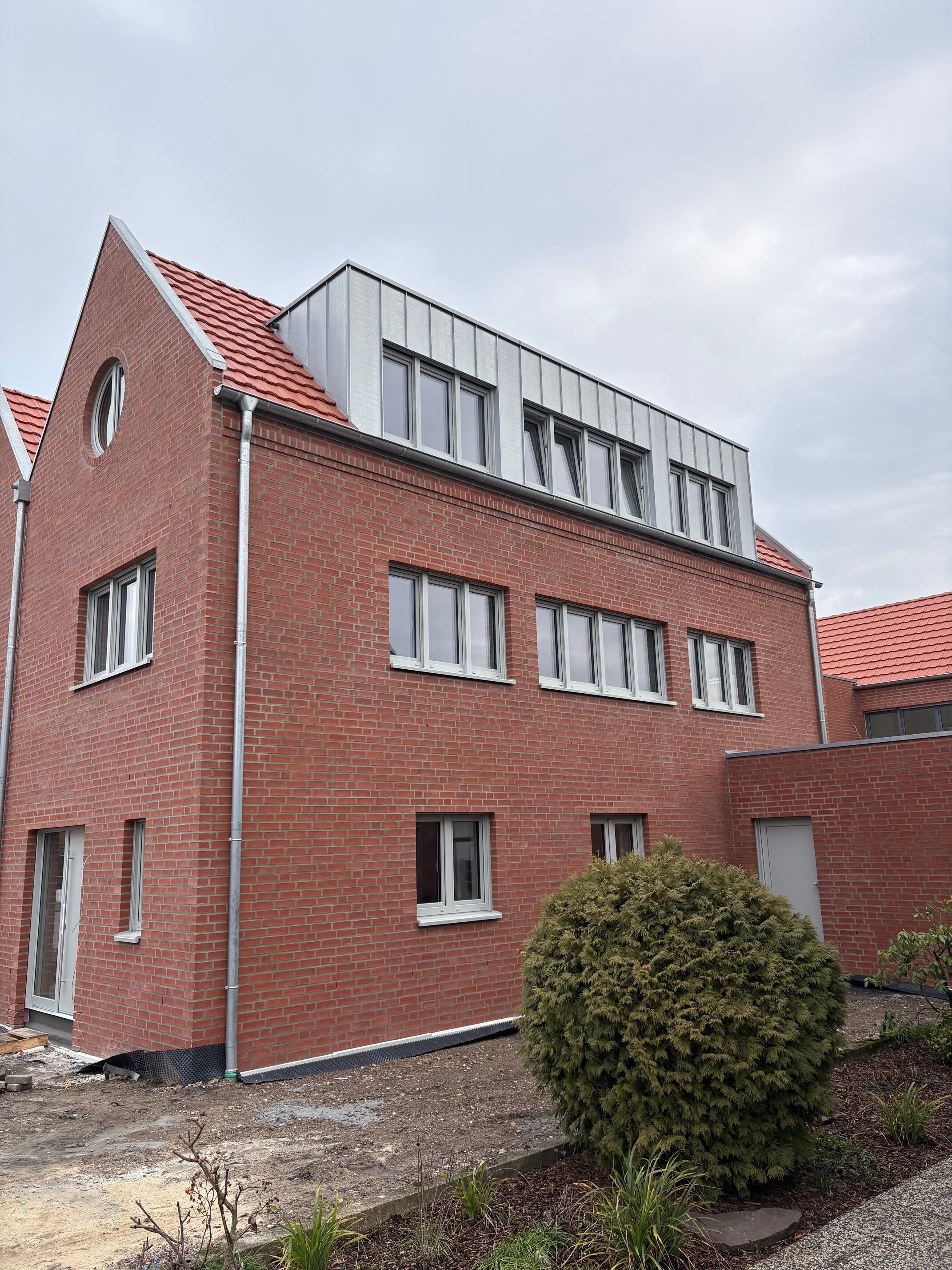 Ein modernes Backsteinhaus mit rotem Dach und auffälligen silbernen Gaubenfenstern