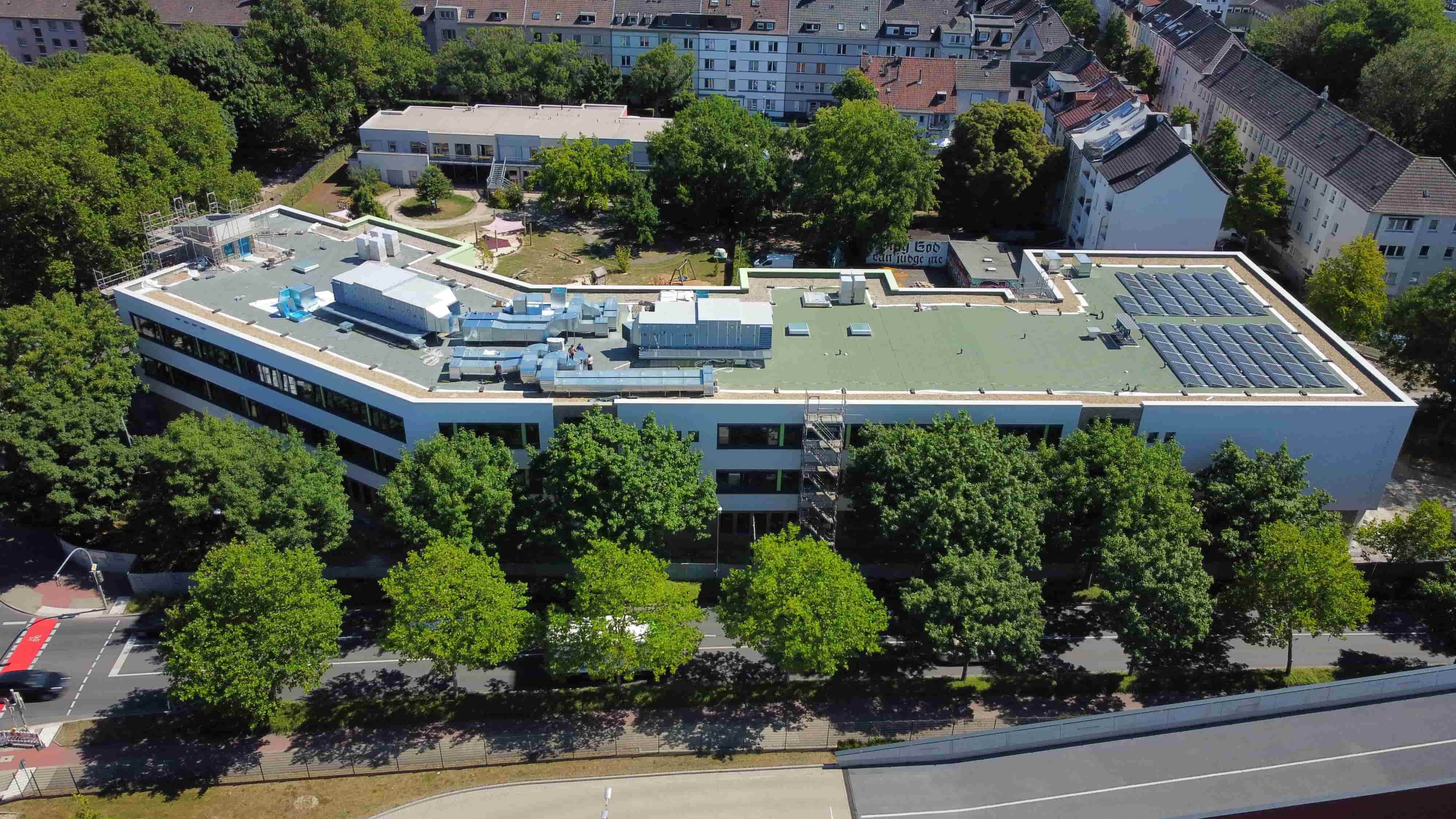 Ein modernes weißes Gebäude mit Solarpanels auf dem Dach ist von grünen Bäumen umgeben