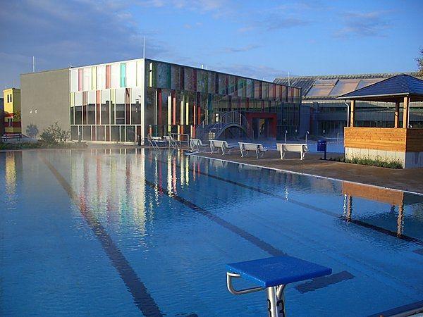 Modern Schwimmhalle mit bunten Fassaden und spiegelndem Außenbecken im Sonnenlicht