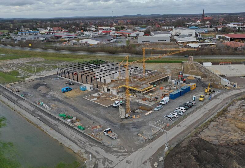 Große Baustelle mit gelbem Kran und mehreren Fahrzeugen neben halbfertigem Gebäude