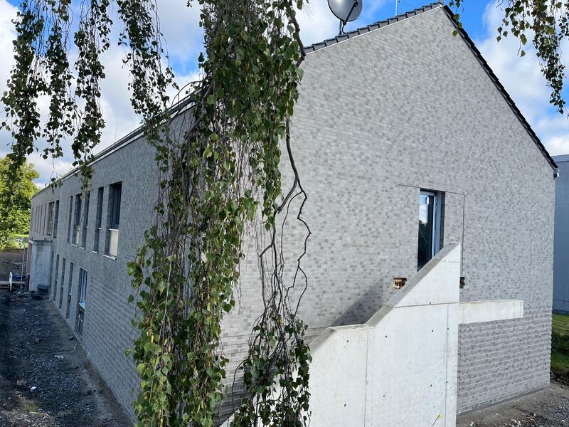 Ein modernes graues Backsteingebäude mit großen Fenstern und hängenden grünen Zweigen