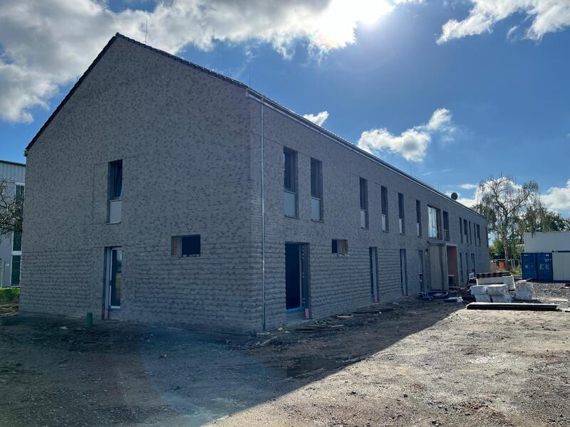 Ein modernes, graues Reihenhaus mit vielen Fensteröffnungen steht im Sonnenlicht