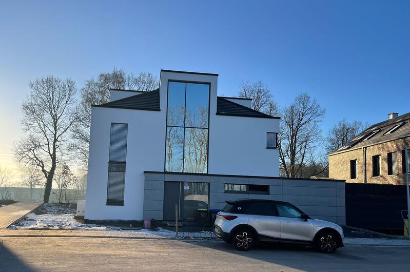 Modernes weißes Haus mit großen Fenstern, schwarzem Dach und geparktem silbernen Auto