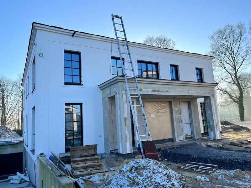 Ein weißes modernes Haus im Bau mit schwarzen Fensterrahmen und einer großen Leiter