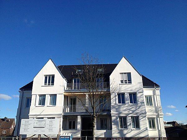 Modern weißes Mehrfamilienhaus mit dunklem Dach vor wolkenlosem blauen Himmel