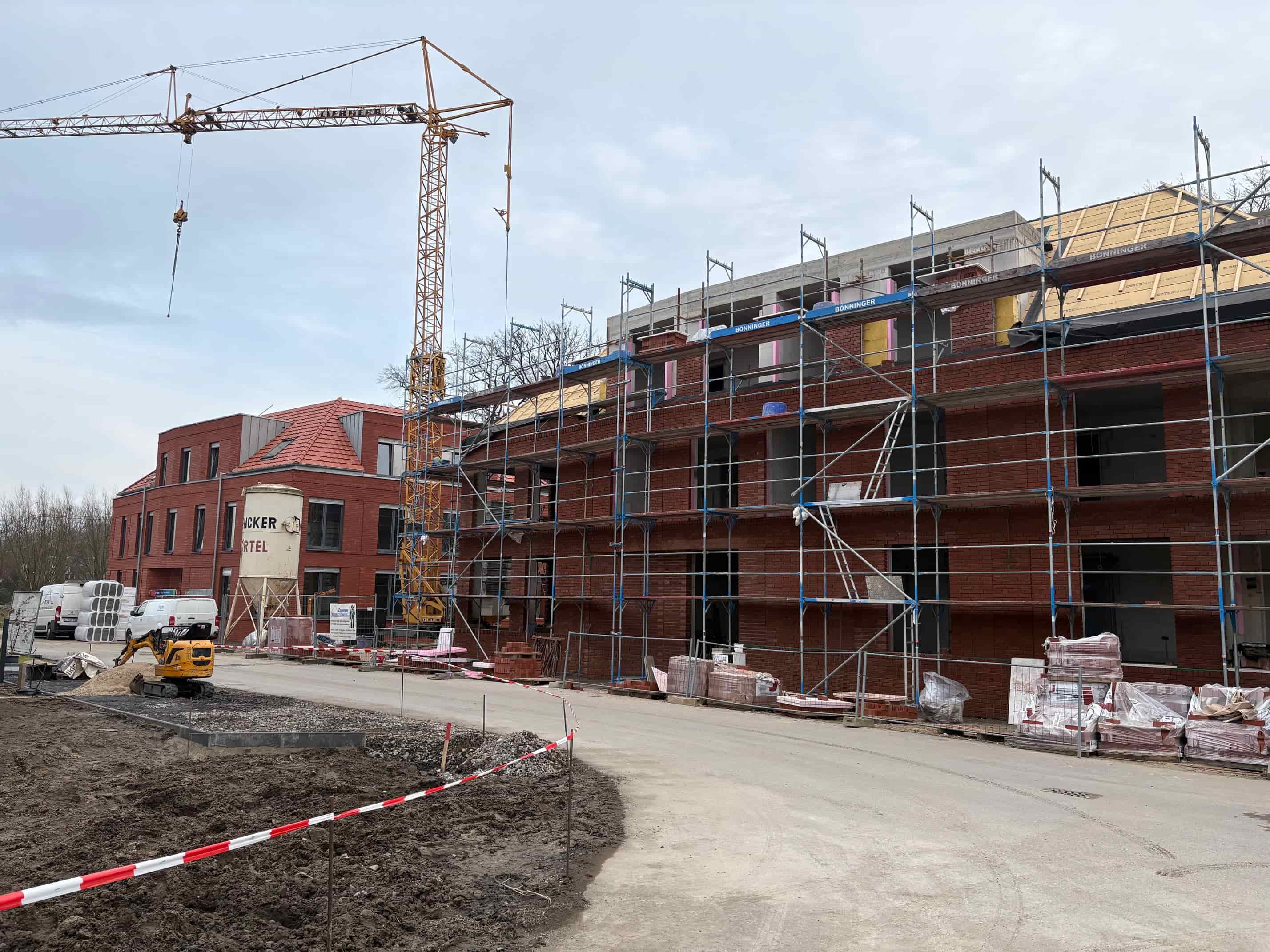 Ein mehrstöckiges Gebäude im Bau mit rotem Backstein und Gerüst vor grauem Himmel