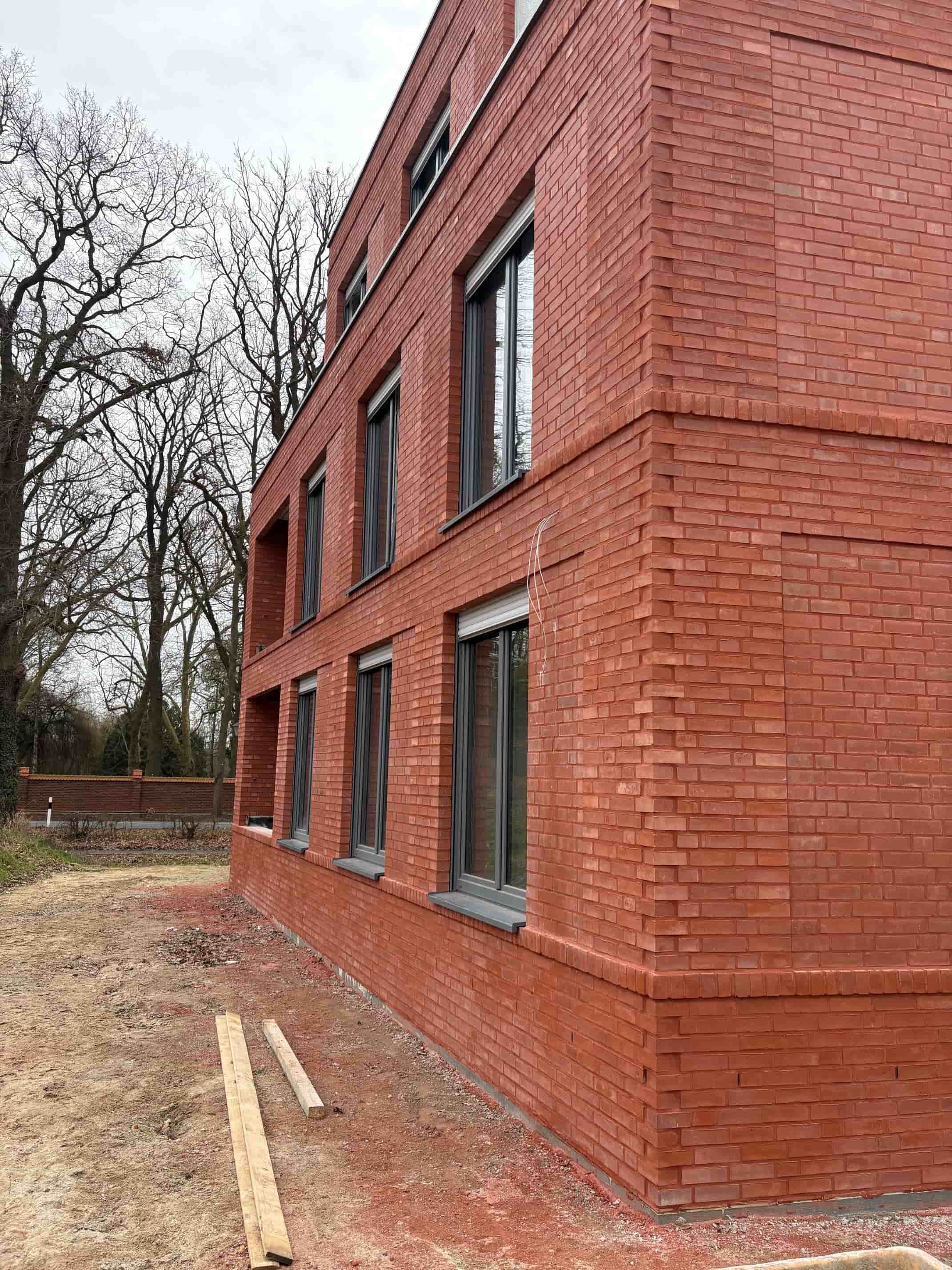 Ein modernes rotes Backsteingebäude mit großen Fenstern und kahlen Bäumen im Hintergrund