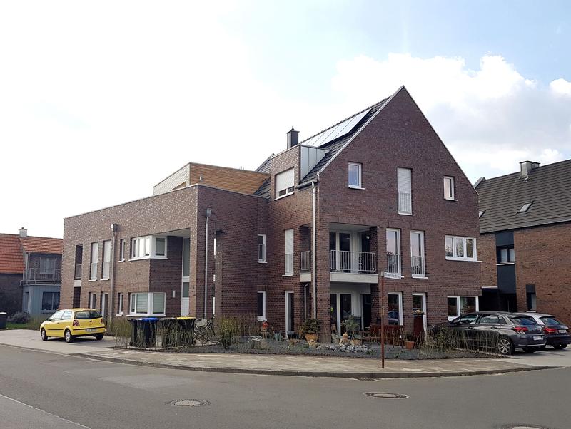 Modernes Backsteingebäude mit großen Fenstern, Balkonen und geparkten Autos davor