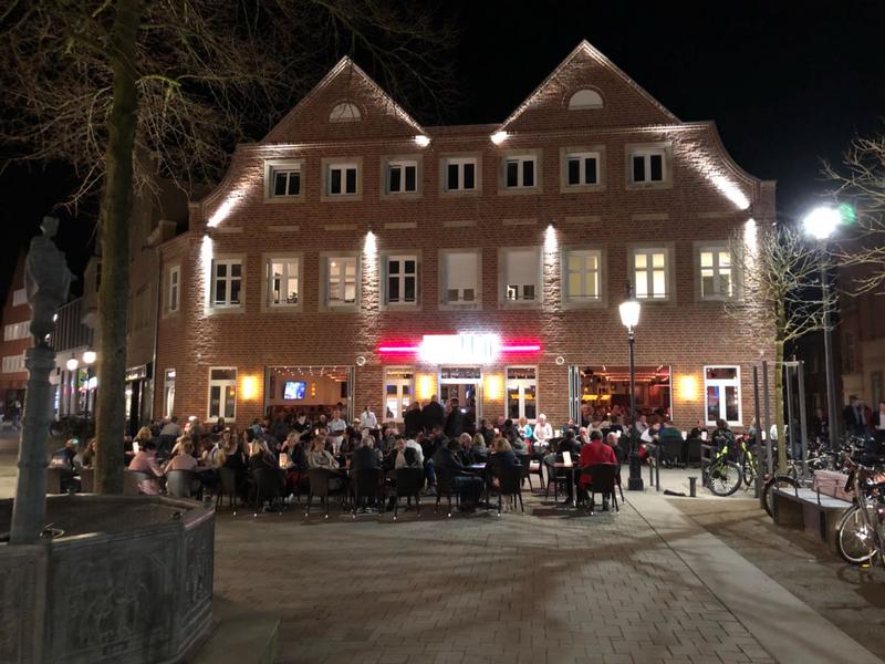Ein belebtes Restaurant mit roten Backsteinen und vielen Menschen draußen bei Nacht