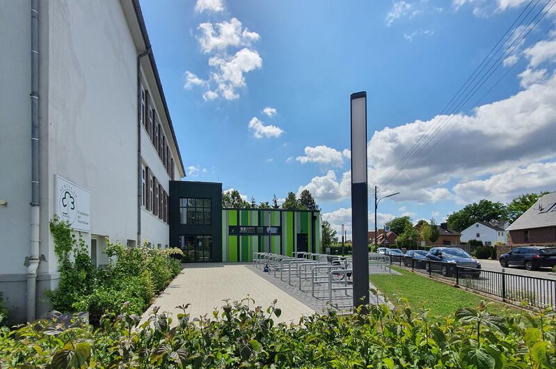 Ein modernes Schulgebäude mit grün gestreifter Fassade, Fahrradständern und blauem Himmel