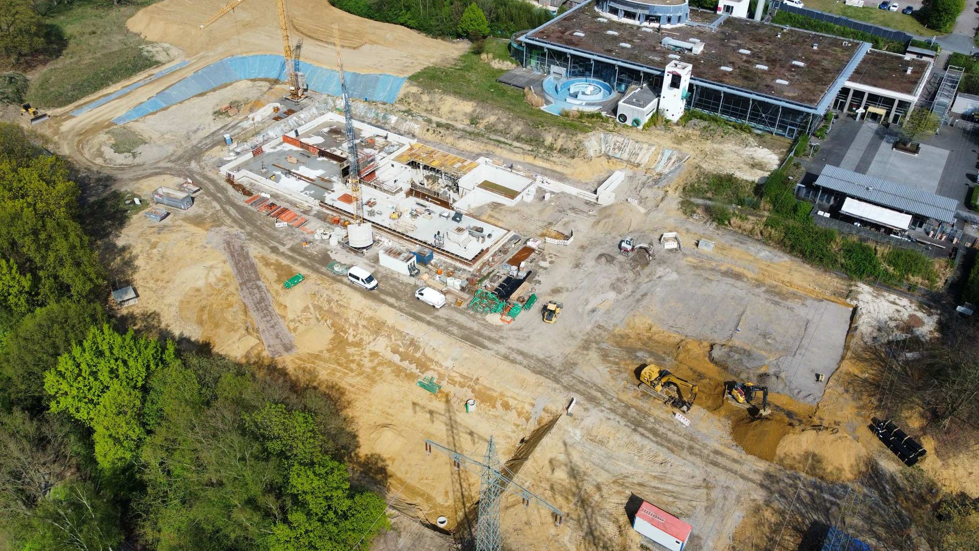 Eine Baustelle mit Baufahrzeugen und einem halbfertigen Gebäude auf sandigem Boden