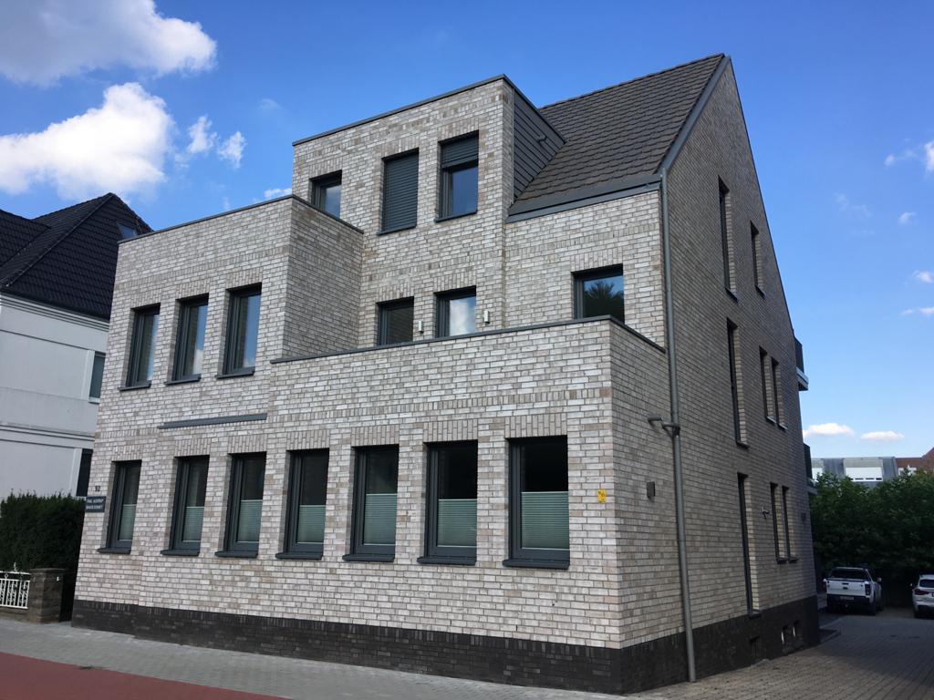 Ein modernes dreistöckiges Eckhaus aus hellem Klinker mit vielen Fenstern und Flachdach
