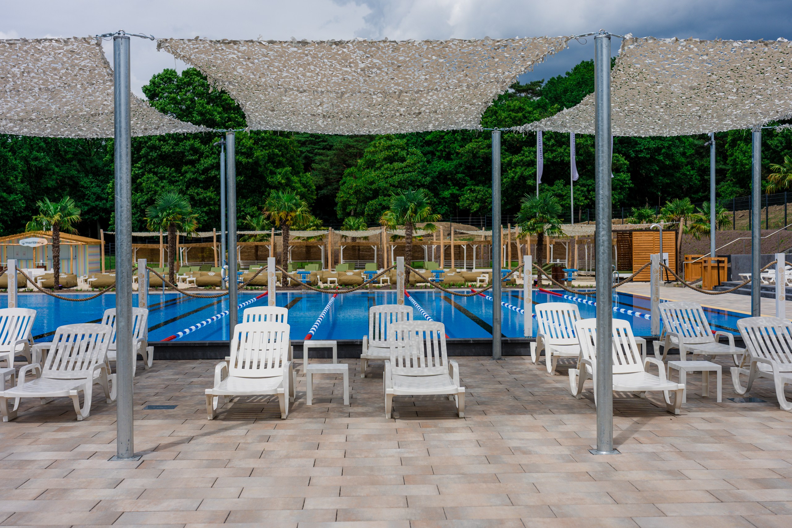 Leeres Freibad mit blauen Bahnen, weissen Liegen und Sonnensegeln