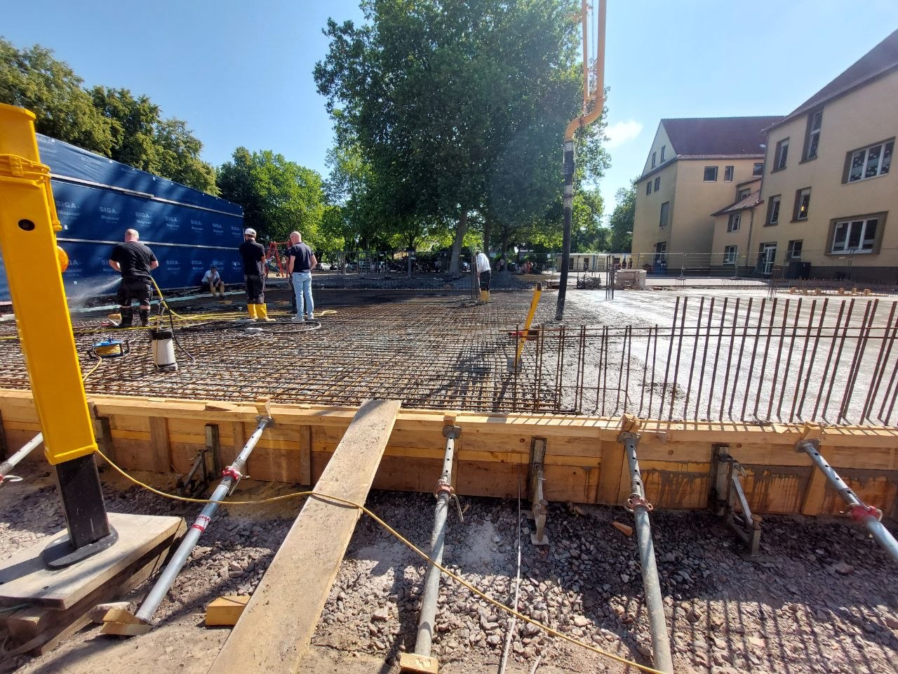 Mehrere Arbeiter mit neutralem Blick an grauer Baustelle mit Kran