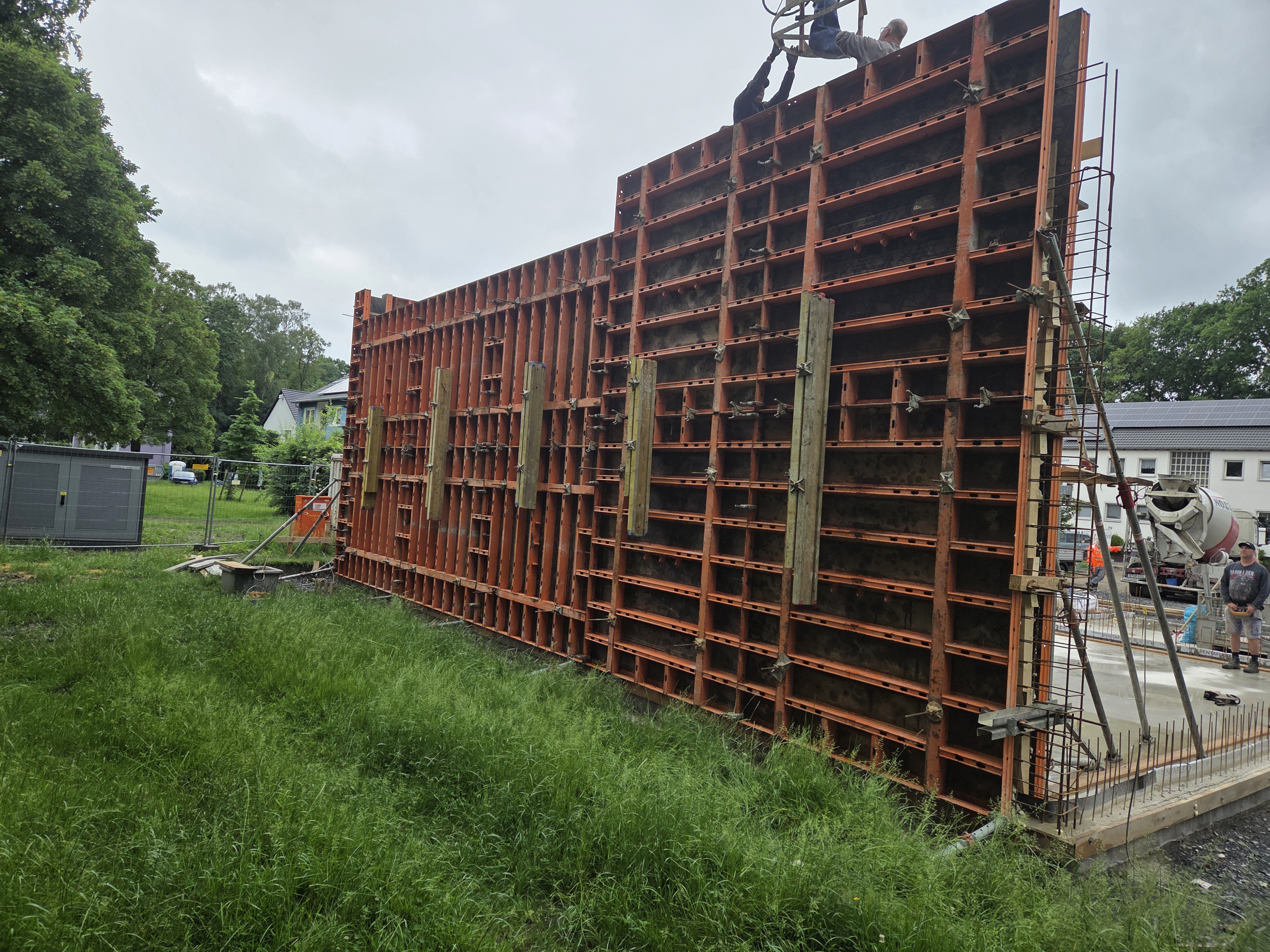 Große orange Schalung am Bau, keine Personen, auffällige Metallgitter und Kranhaken oben