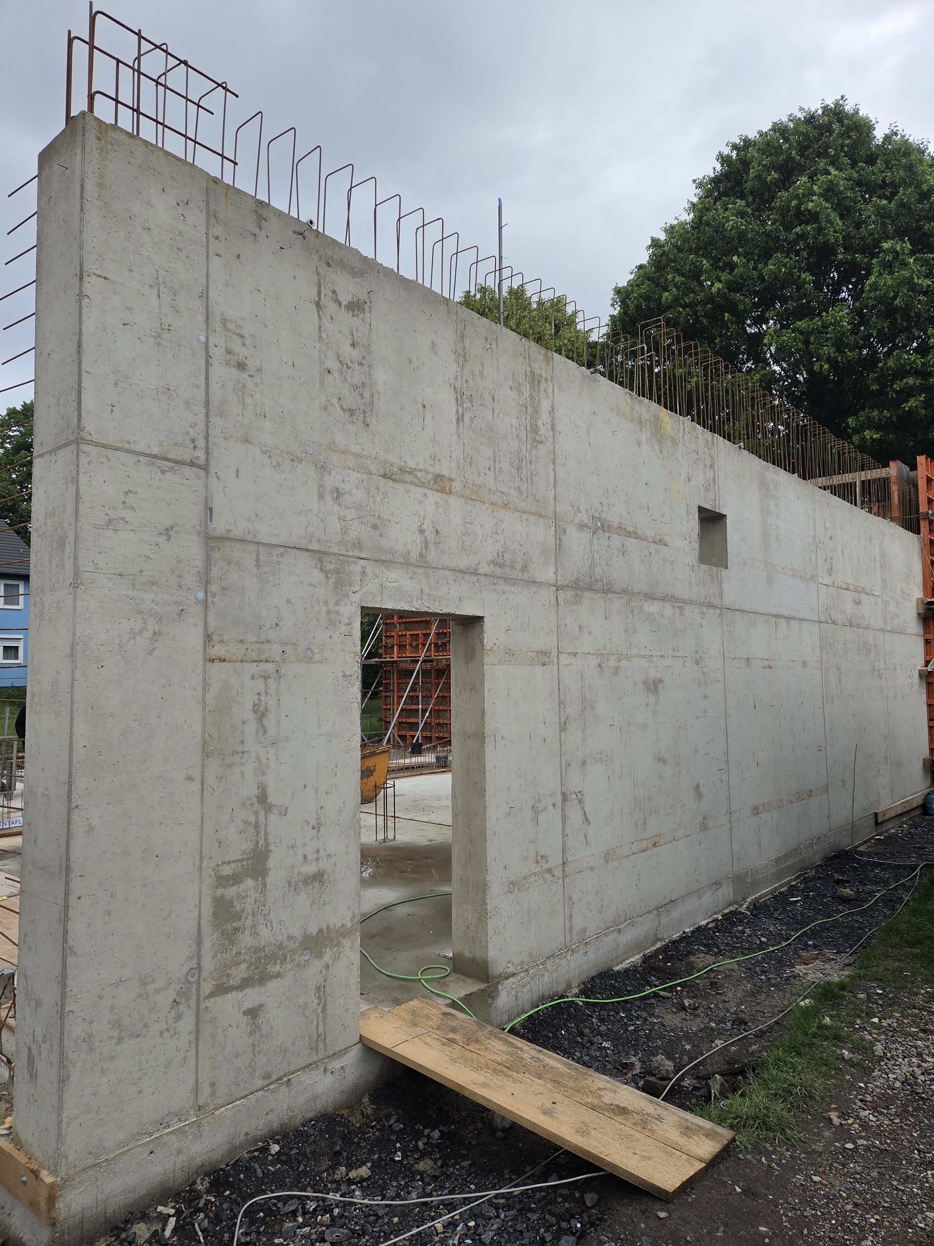 Glatte graue Betonwand im Bau, nüchtern, mit Türöffnung und Stahlstäben